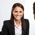 **Confident Job Interviewee:** A well-dressed individual with excellent posture, smiling genuinely during a job interview. The background should be a professional office setting. Focus on conveying confidence and approachability.